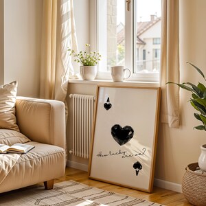 May include: A framed print with a black and white design of a playing card. The card is the Ace of Spades and features a large black heart in the center. The text "How lucky are we?" is written in cursive below the heart.