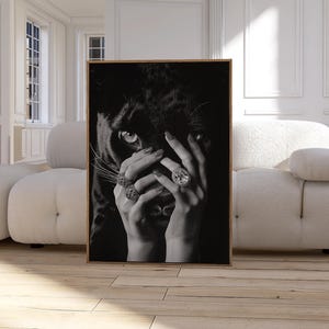 May include: Black and white photo of a woman's hands covering her face. The woman is wearing rings with large gemstones. The background is a black panther.
