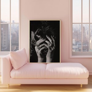 May include: Black and white photograph of a woman's hand covering her face, with a black panther's face peeking out from behind her fingers. The woman is wearing several rings with large gemstones.