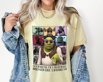 May include: A yellow t-shirt with a colorful collage of Shrek characters. The text "Cuz darling I'm a nightmare dressed like a daydream" is printed on the bottom of the shirt.