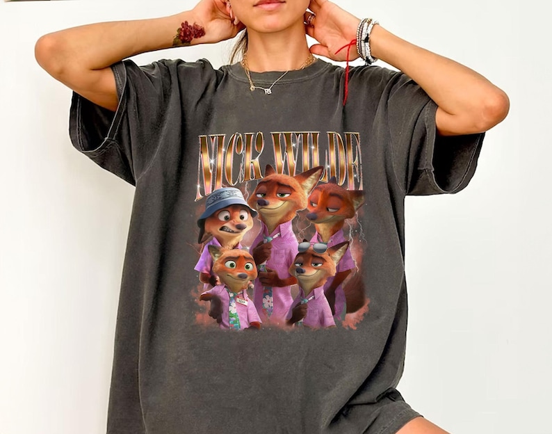 May include: Dark gray t-shirt featuring a graphic of Nick Wilde from Zootopia. The image shows Nick Wilde and other fox characters wearing pink shirts. The text "NICK WILDE" is printed above the image in gold.