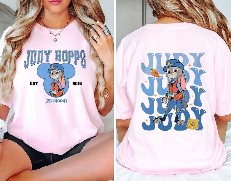 May include: Pink t-shirt featuring a cartoon graphic of Judy Hopps from Zootopia. The front design includes the text "JUDY HOPPS" above an image of Judy, with "EST. 2016" and "ZOOTOPIA" below. The back has a repeating "JUDY" design and Judy Hopps.