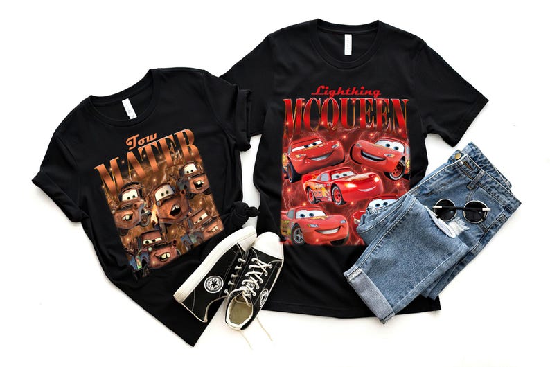 May include: Two black t-shirts with graphic designs, one featuring Tow Mater and the other Lightning McQueen from the Cars movie. The image also includes a pair of blue jeans, black sneakers, and sunglasses.