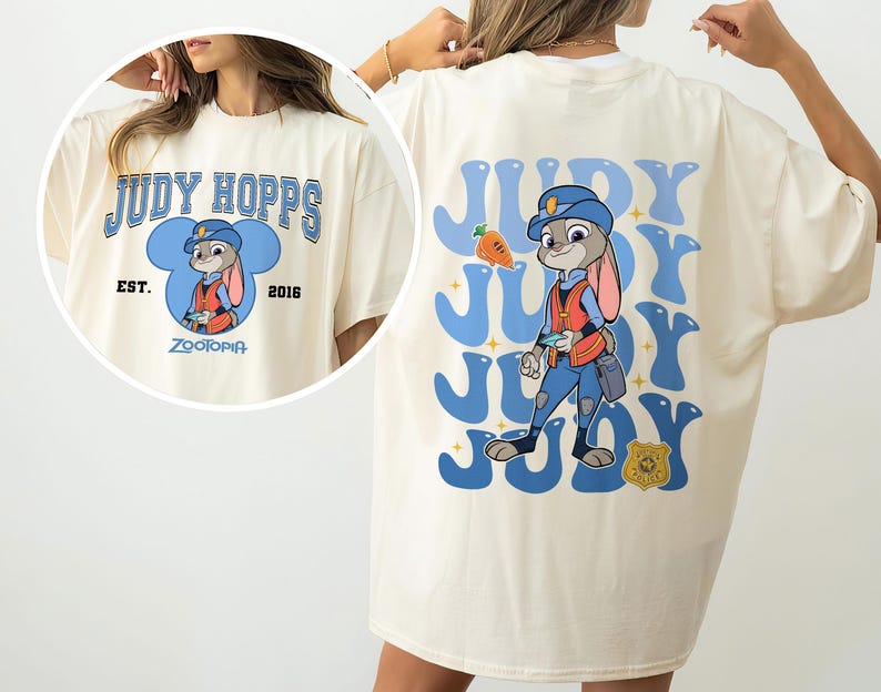 May include: Cream-colored t-shirt featuring a cartoon illustration of Judy Hopps from Zootopia. The front design includes the text "JUDY HOPPS" above a character image, with "EST. 2016" and "Zootopia" below. The back displays a larger Judy Hopps graphic.