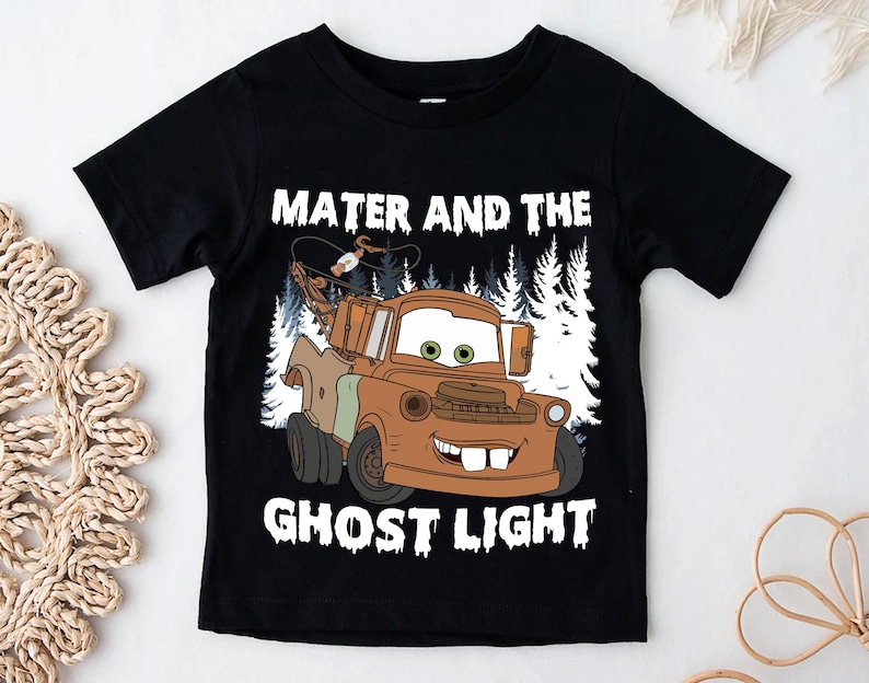May include: Black short-sleeved t-shirt with a cartoon image of Mater from the film Cars. The image shows Mater in brown and tan with a forest backdrop. The text "Mater and the Ghost Light" is printed above and below the image in white lettering.