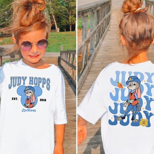 May include: White t-shirt featuring a cartoon image of Judy Hopps from Zootopia. The front of the shirt has the text "JUDY HOPPS" and "ZOOTOPIA". The back of the shirt has a larger image of Judy Hopps with the text "JUDY".