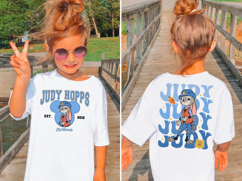 May include: White t-shirt featuring a cartoon image of Judy Hopps from Zootopia. The front of the shirt has the text "JUDY HOPPS" and "ZOOTOPIA". The back of the shirt has a larger image of Judy Hopps with the text "JUDY".