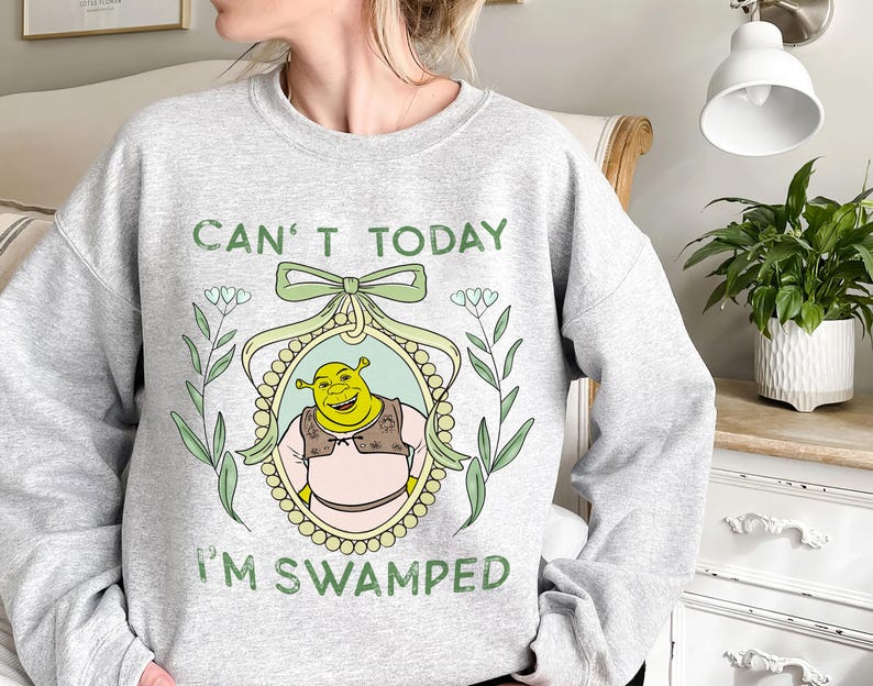 Puede incluir: Sudadera gris con un personaje de dibujos animados de ogro verde en un marco con el texto "Can't Today I'm Swamped".