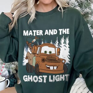May include: Dark green sweatshirt with a cartoon image of Mater from the film Cars, and the text "Mater and the Ghost Light" in white. The image shows Mater as a brown tow truck with a smiling face, set against a backdrop of white trees.