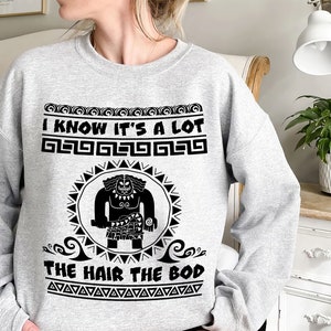 May include: Gray sweatshirt with a black graphic of a cartoon character with the text "I know it's a lot the hair the bod" and a repeating pattern of geometric shapes.