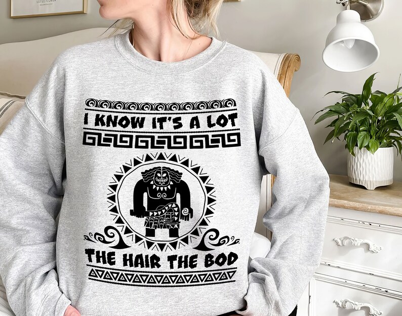 May include: Gray sweatshirt with a black graphic of a cartoon character with the text "I know it's a lot the hair the bod" and a repeating pattern of geometric shapes.
