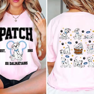 Op de afbeelding: Roze T-shirt met een zwarte afbeelding van een Dalmatiër met de tekst "PATCH EST. 1961 101 DALMATIANS" op de voorkant. De achterkant van het shirt heeft een afbeelding van meerdere Dalmatiërs in verschillende poses.