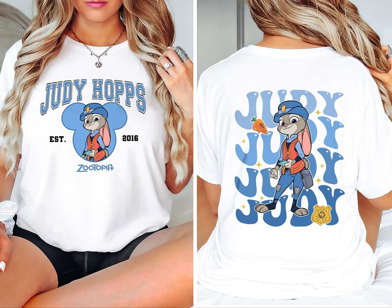 May include: White t-shirt featuring a cartoon graphic of Judy Hopps from Zootopia. The front design includes the text "JUDY HOPPS" above an image of Judy in a police uniform, with "EST. 2016" and "ZOOTOPIA" below. The back has a repeating Judy design.