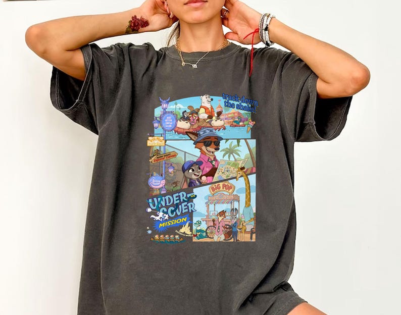May include: Dark gray t-shirt featuring a colorful cartoon graphic with the words "Undercover Mission" and "Track Down the Shakes". The graphic depicts various cartoon characters in a comic book style.