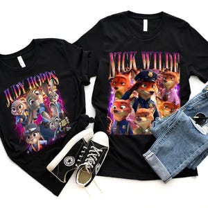 May include: Two black t-shirts featuring characters from the film Zootropolis. One shirt displays "Judy Hopps", the other "Nick Wilde". The image also includes black trainers, blue jeans, and sunglasses.