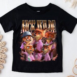 May include: Black t-shirt featuring a graphic of Nick Wilde from Zootopia. The image shows Nick Wilde and other fox characters wearing pink shirts. The text "NICK WILDE" is printed in gold letters above the image.