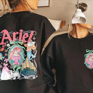 Pu&ograve; includere: Felpa nera con una stampa grafica colorata di Ariel de La Sirenetta. La grafica include Ariel, Re Tritone, Flounder e Sebastian. Il testo "Ariel" e "La Sirenetta" sono anche inclusi nella grafica.