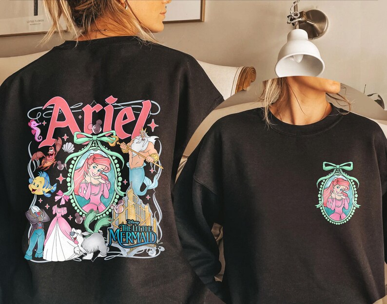 Pu&ograve; includere: Felpa nera con una stampa grafica colorata di Ariel de La Sirenetta. La grafica include Ariel, Re Tritone, Flounder e Sebastian. Il testo "Ariel" e "La Sirenetta" sono anche inclusi nella grafica.