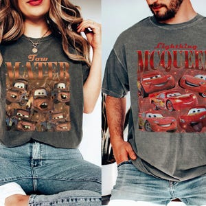 May include: Two gray t-shirts featuring graphics from the animated movie "Cars." One shirt displays Tow Mater with text, while the other showcases Lightning McQueen. Both shirts have a vintage, distressed look.