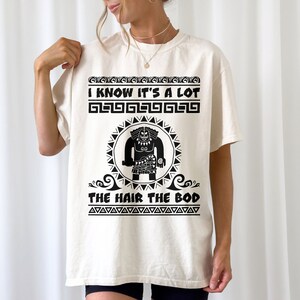 May include: A white t-shirt with a black graphic print of a cartoon character with the text "I know it's a lot, the hair the bod".