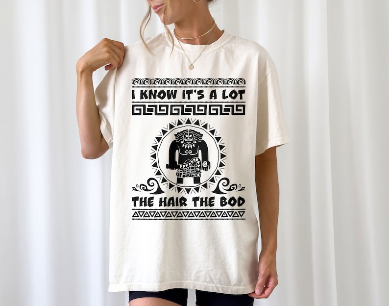 May include: A white t-shirt with a black graphic print of a cartoon character with the text "I know it's a lot, the hair the bod".