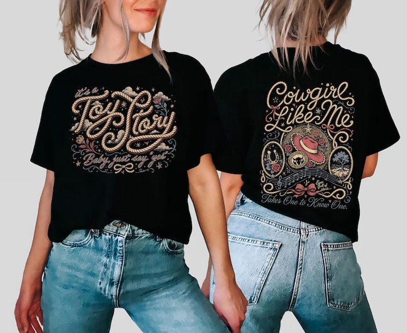 May include: A black t-shirt featuring a graphic design on the front and back. The front displays the text "It's a Toy Story, Baby, just say yet" in rope-style lettering. The back features the text "Cowgirl Like Me" and "Takes One to Know One".
