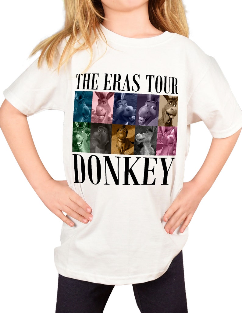 Pode incluir: Camiseta branca com um gr&aacute;fico preto de Donkey de Shrek. O gr&aacute;fico apresenta uma colagem do rosto de Donkey de diferentes filmes da franquia Shrek. Os textos "The Eras Tour" e "Donkey" est&atilde;o impressos em preto.