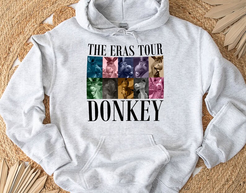 Pode incluir: Camisola de moletom cinza com capuz com um gr&aacute;fico de Donkey de Shrek. O gr&aacute;fico apresenta uma colagem do rosto de Donkey em diferentes express&otilde;es. O texto "The Eras Tour" e "Donkey" est&atilde;o impressos em preto.
