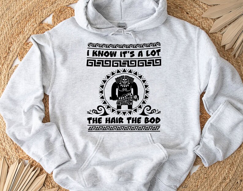 May include: Gray hooded sweatshirt with a black graphic print of a cartoon character with the text "I know it's a lot the hair the bod" printed on the front.