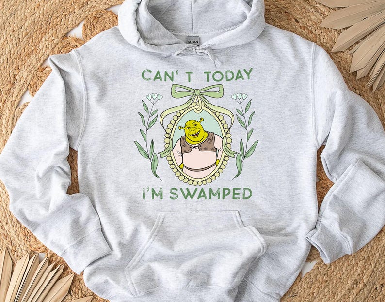 Puede incluir: Una sudadera con capucha gris con el texto "Can't today I'm swamped" y una imagen de dibujos animados de Shrek en un marco con flores.