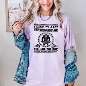 May include: A lavender t-shirt with a black graphic of a cartoon character with the text "I know it's a lot the hair the bod".