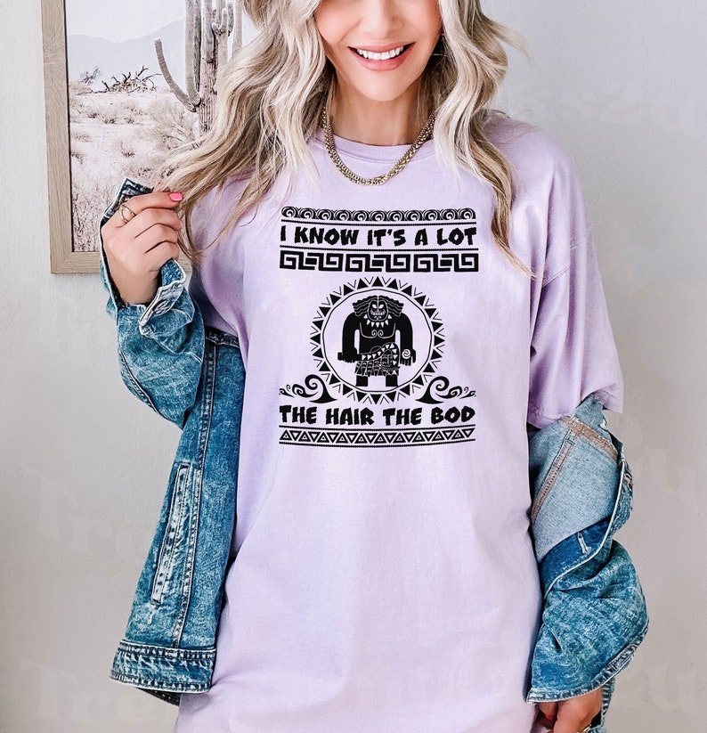 May include: A lavender t-shirt with a black graphic of a cartoon character with the text "I know it's a lot the hair the bod".