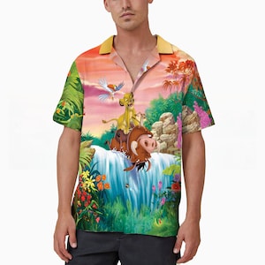 May include: A short-sleeved button-up shirt with a colorful print featuring Simba, Pumbaa, and Zazu from Disney's The Lion King. The print depicts a jungle scene with a waterfall and lush greenery.
