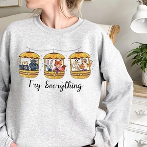 Pode incluir: Camisola cinza claro com um gr&aacute;fico de tr&ecirc;s g&ocirc;ndolas amarelas, cada uma com animais de desenho animado. O texto "Try Everything" est&aacute; impresso em escrita preta abaixo. A camisola &eacute; de gola redonda.