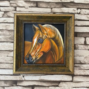 May include: A framed painting of a brown horse's head with a white stripe on its face. The horse is looking to the left, and the painting is set against a dark background.