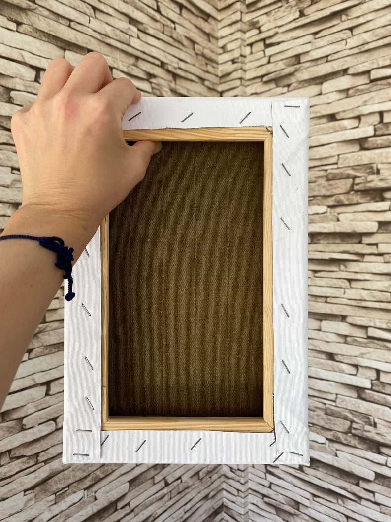 May include: The back of a stretched canvas with a wooden frame. The canvas is white and has been stapled to the frame. The frame is made of natural wood.