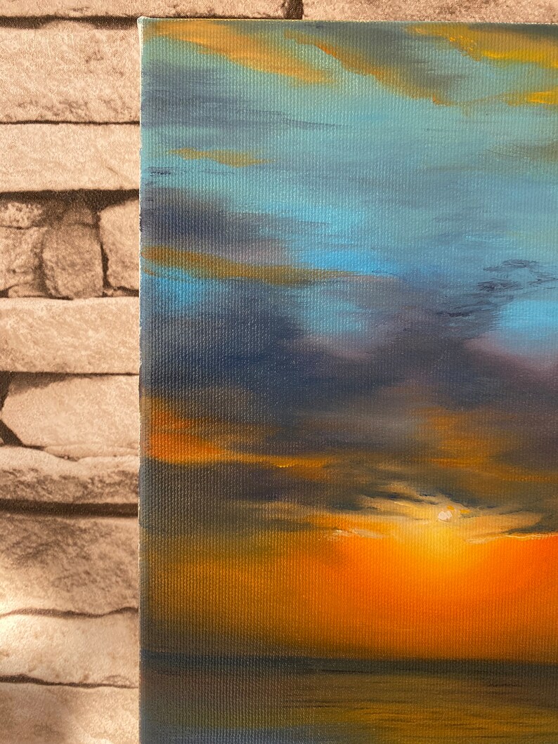May include: A painting of a sunset over the ocean. The sky is a mix of blue, purple, and orange, with clouds reflecting the light of the setting sun. The water is a dark blue, reflecting the sky above.