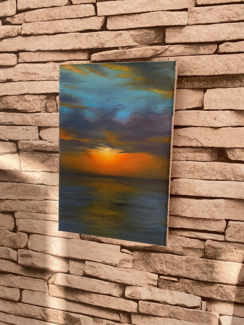May include: A painting of a sunset over the ocean. The sky is a mix of blue, purple, and orange, with clouds reflecting in the water. The sun is setting in the distance, casting a warm glow over the scene.
