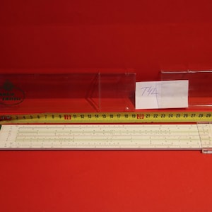 May include: A white slide rule with green end caps and a yellow measuring tape. The slide rule is labeled "742".