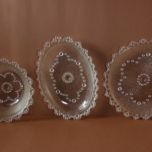 May include: Three clear glass plates with a decorative, raised, beaded edge. The plates have a textured surface with a pattern of small circles.