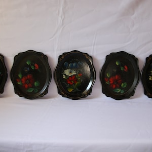 May include: Five black oval-shaped trays with scalloped edges. Each tray is hand-painted with a floral design in shades of red, blue, white, and green.