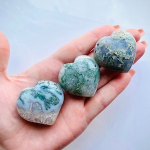 May include: Three green and white moss agate heart shaped stones. The stones are polished and have a smooth, natural finish.