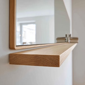 May include: A rectangular wooden framed mirror with a matching shelf. The mirror and shelf are made of light-colored wood, possibly oak, and are mounted on a white wall. The shelf is approximately 30 inches long.