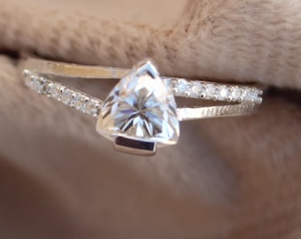 May include: A silver ring with a triangular-shaped diamond set in the center. The ring has a delicate band with small diamonds set along the sides.