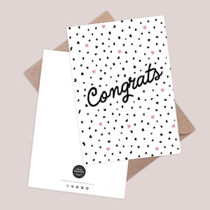 Puede incluir: Una tarjeta de felicitación blanca con lunares negros y corazones rosas, con la palabra "Congrats" en escritura negra. La tarjeta se combina con un sobre blanco en blanco y un sobre marrón.