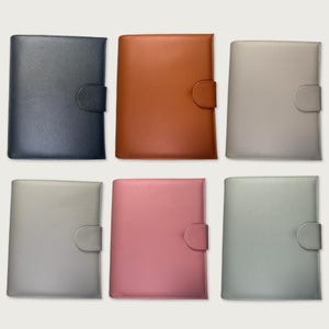 Puede incluir: Una colección de seis agendas rectangulares con un acabado texturizado y granulado. Cada agenda cuenta con un cierre de lengüeta redondeado en el lado derecho. Los colores incluyen azul oscuro, naranja, beige claro, gris claro, rosa viejo y verde salvia.