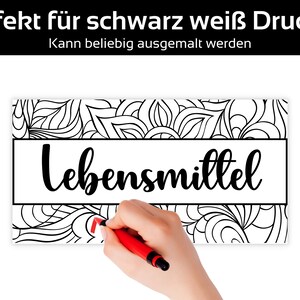 May include: Black and white coloring page with the word "Lebensmittel" in a rectangular box. The background features a floral design. The text at the top says "Perfekt f&uuml;r schwarz wei&szlig; Drucker" and "Kann beliebig ausgemalt werden". A hand is drawing with a red marker.