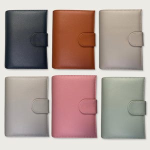 Puede incluir: Seis agendas rectangulares con un acabado de textura granulada, cada una con un cierre de lengüeta lateral a juego. El conjunto incluye colores azul marino oscuro, marrón cálido, beige claro, gris suave, rosa empolvado y verde salvia, dispuestos en dos filas.