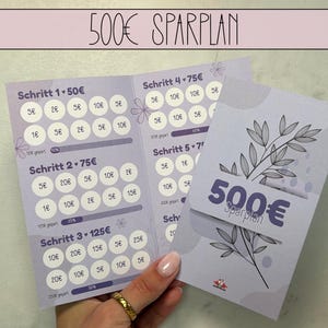 Peut inclure: Un suivi d'épargne violet clair avec le texte "500€ SPARPLAN" en haut. Le suivi comporte plusieurs sections avec des cercles pour marquer les objectifs d'épargne. Une main tient le suivi, et une carte séparée avec le même texte.