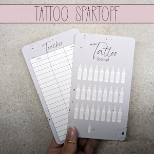 Op de afbeelding: Twee grijze kaarten met zwarte inkt. De kaart links is een tattoo-tracker met het woord "Tracker" bovenaan en kolommen voor "Datum" en "Samenvatting". De kaart rechts is een tattoo-inktkaart met de woorden "Tattoo Spartopf" bovenaan en 36 kleine inktflespictogrammen.